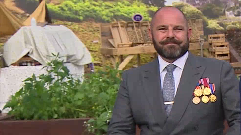 James Kaye, who has a beard and is in a grey suit decorated with five medals