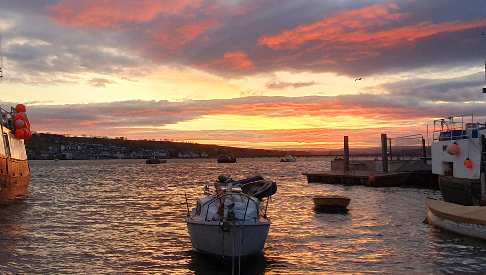 Boats docked in Teignmouth. Clouds are in the sky, which has a yellow and orange hue to it.