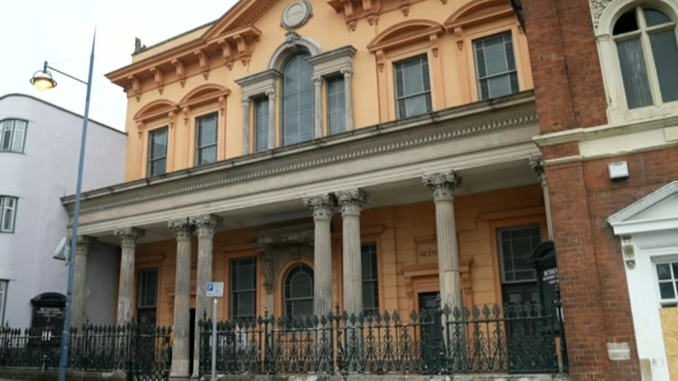 Outside image of the building painted light orange, with concrete columns and windows