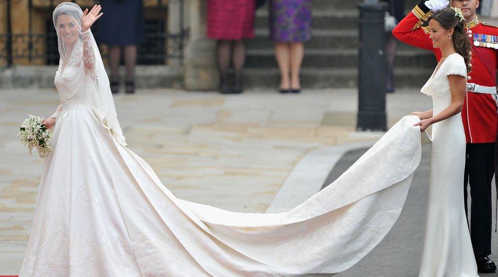 Catherine Middleton waves as she walks towards Westminster Abbey with Pippa Middleton holding her train.