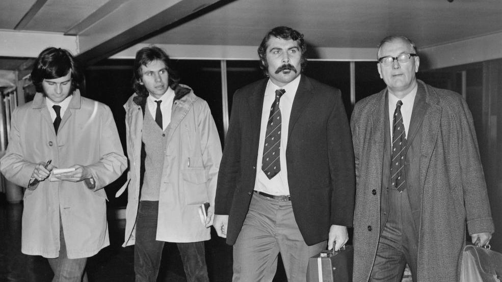 New Zealand rugby union player Keith Murdoch (1943-2018) is third from left, wearing a tie and black blazer, in London as he leaves the country early to return to New Zealand on 5th December 1972