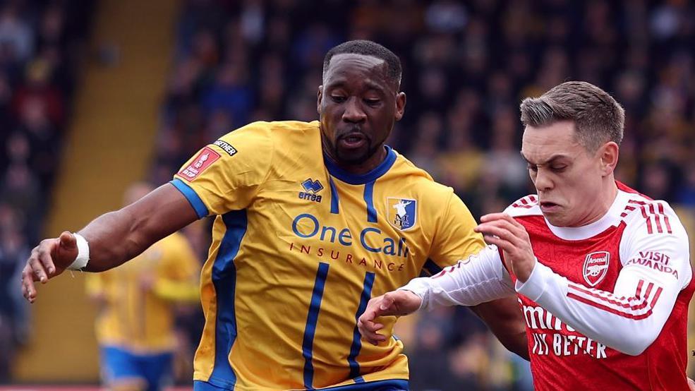 Lucas Akins of Mansfield Town and Leandro Trossard of Arsenal battle for possession