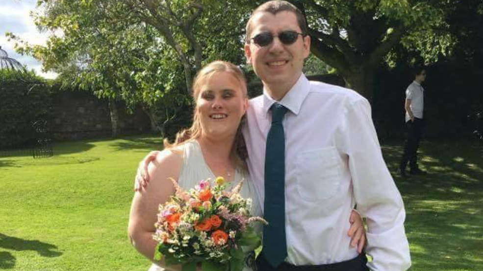 Kate Healey holding flowers next to her partner Mike in a white shirt and navy tie