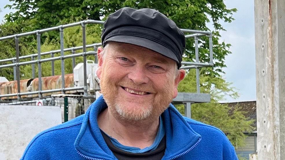 David Goode is standing in front of the closed lock at Baits Bite. Behind him is a large red 'lock closed' sign. David is wearing a blue fleece, black cap and black top. He has grey and ginger facial hair.