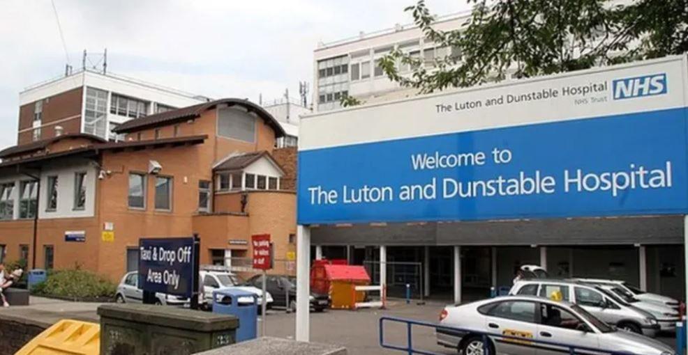 Front of a hospital showing buildings, cars and a sign