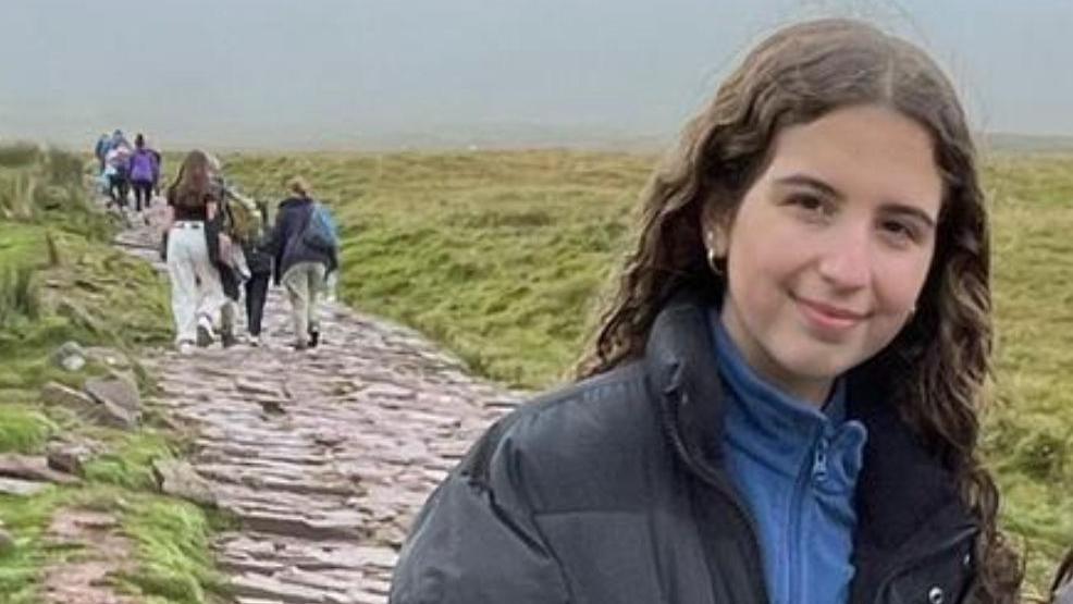 A girl smiling at the camera standing on a mountain path