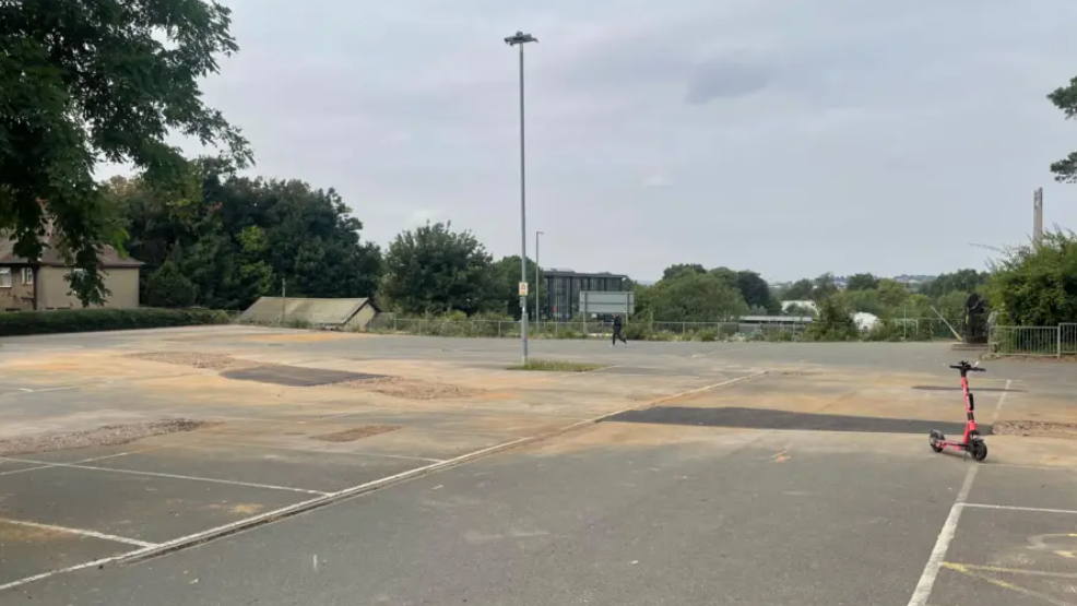 A dusty car park with a red scooter off to the right hand side. 