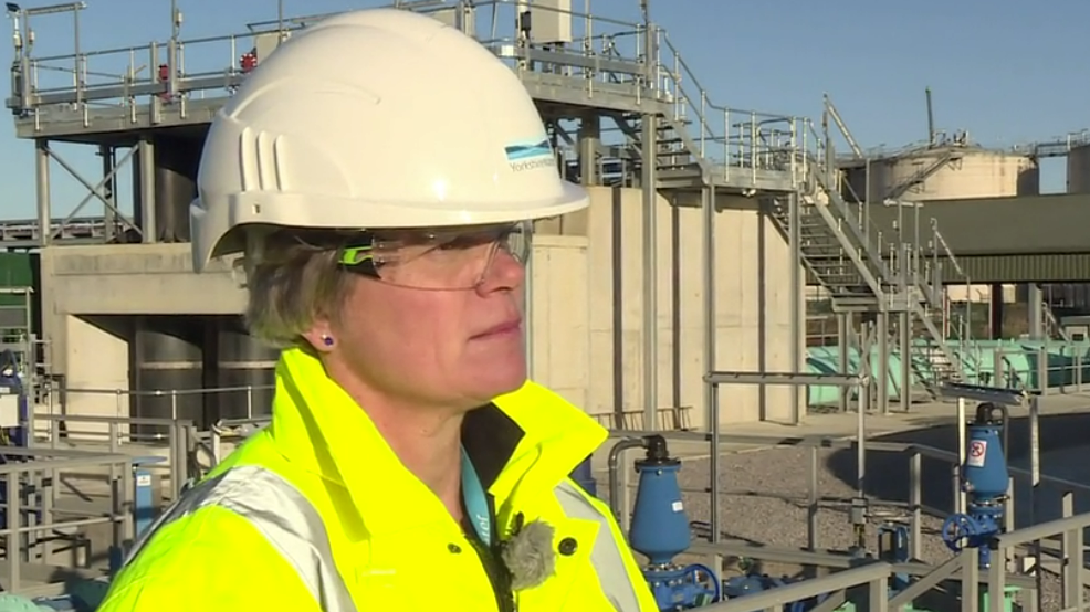 Nicola Shaw in a helmet and high vis jacket stood in front of a sewage works