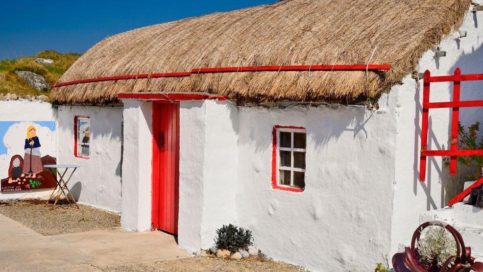 A white thatched cottage with red doors and windows