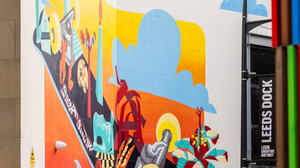 A colourful mural on the side of an apartment block. A sign saying 'Leeds Dock' sits behind it.