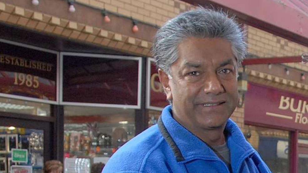 Jake Jacobs smiles as he stands in front of a precinct of shops. He has short, grey hair and wears a blue fleece.