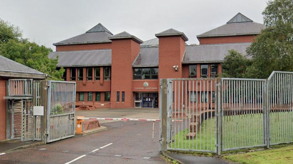 Coleraine Court Office, it is a red brick building with green grass and trees. Silver gates surround it.