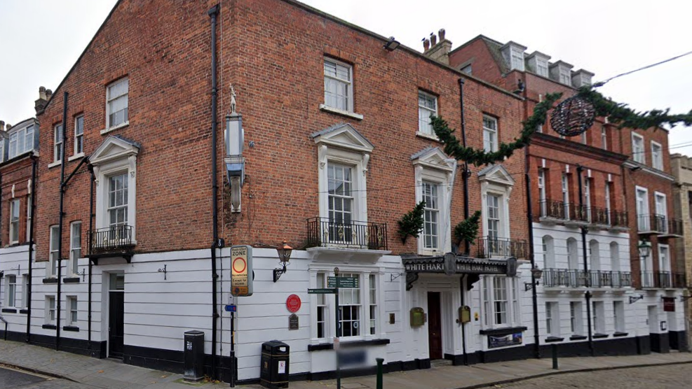 A view of the hotel from higher up on the hill.  The bottom third of the hotel is rendered white, and above the building has red brick.  The white windows are large and elegant.