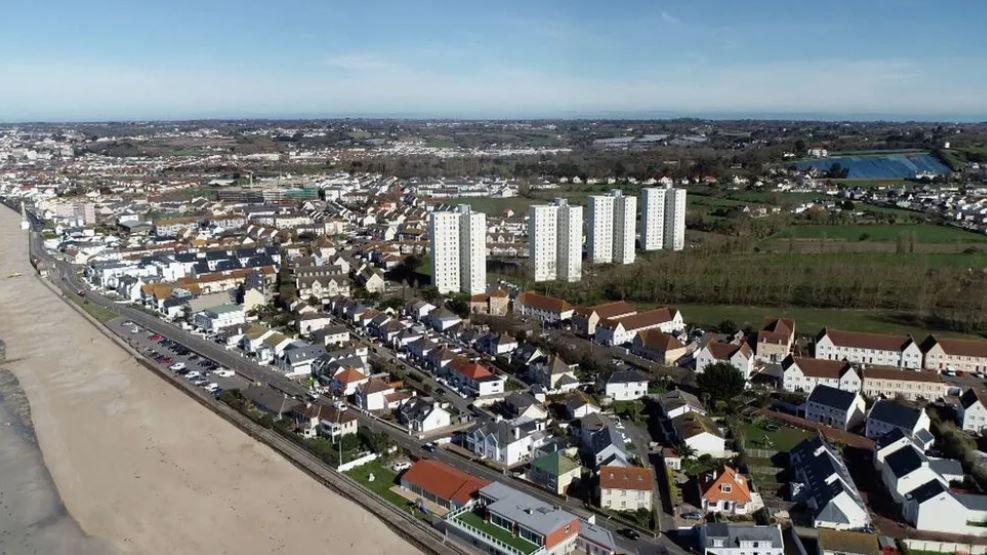 Aerial of housing in Jersey. The majority of the houses are two storey white houses with a slate roof. There are also some high rise flats. All the properties overlook the beach.