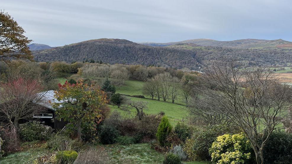 View of fields and mountrains, with leaves in different autumn colours. A dark brown building is pictured to the left 