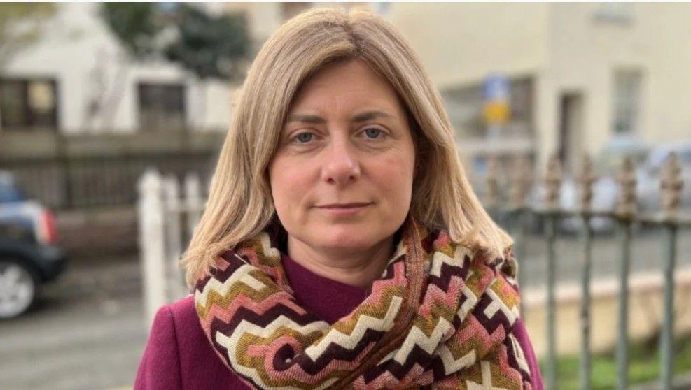 Deputy Lyndsay Feltham is wearing a purple top and a multi-coloured scarf. She has blonde hair.