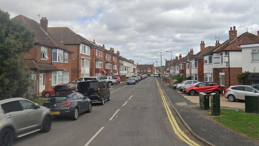 A residential street lined with houses and cars on either side