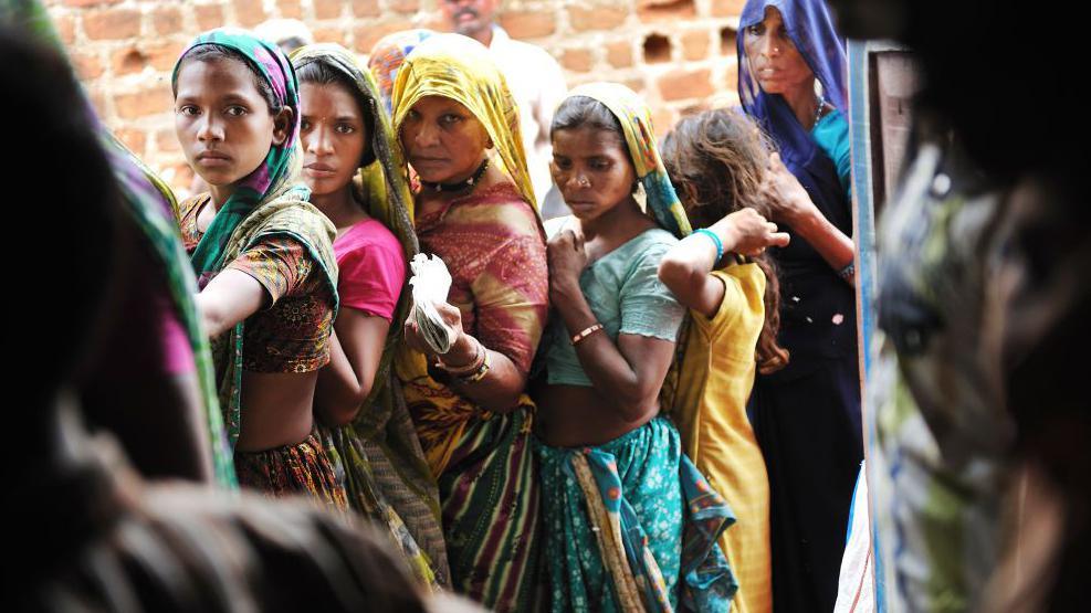 MADHYA PRADESH, INDIA - JULY 2010: A group of Indian women line up outside the Fair Price Shop with their ration cards to receive portions of wheat, sugar, kerosene and rice from the government in Jhabua, Madhya Pradesh, India, on July 16, 2010. T