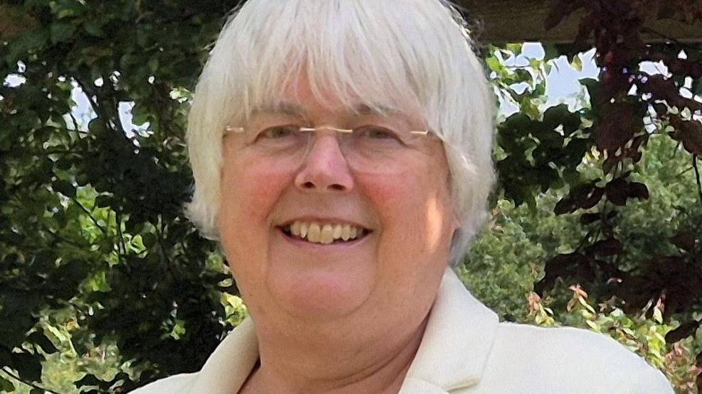 Charlotte Cane wearing a white jacket and clear framed glasses looking at the camera