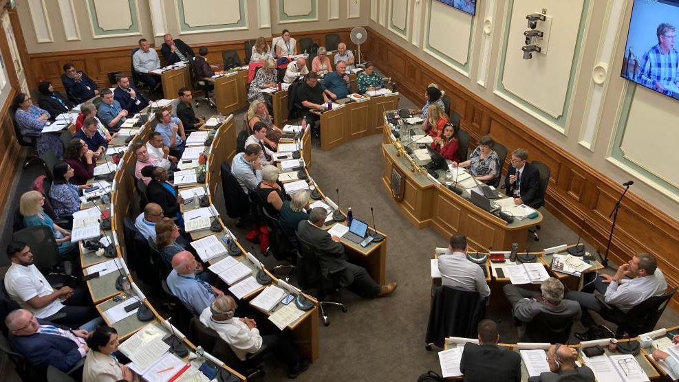 A number of councillors sitting at desks in the council chamber