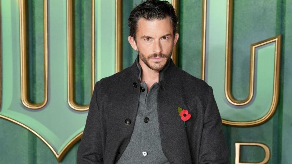 Actor Jonathan Bailey, who reprises his role of Prince Fiyero in the Wicked sequel, is pictured at the film's London premiere looking at the camera. He is wearing a dark grey jacket and Remembrance Day poppy over a grey buttoned top.