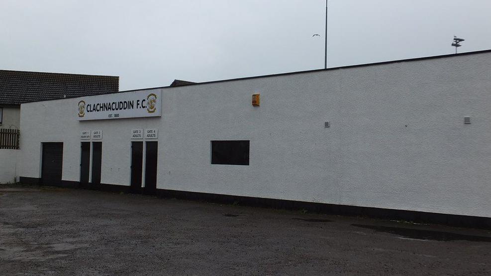 A white wall of the outside of Clachnacuddin's Grant Street Park. There gates into the ground and sign that reads: "Clachnacuddin FC".