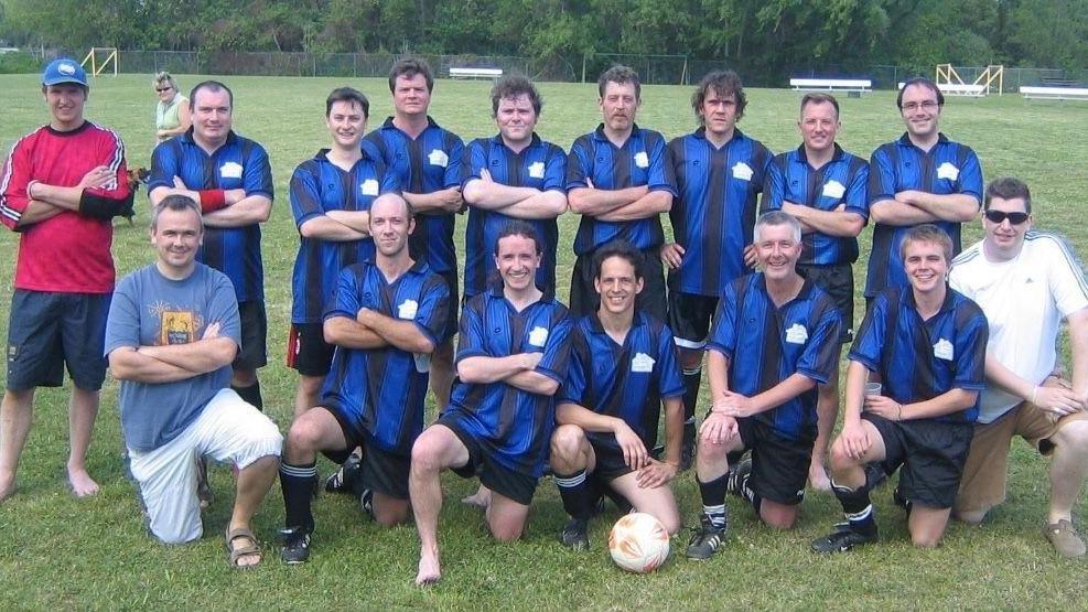 A group of men in the standard football team pre-match photo pose (two rows, with the players in the front row kneeling). The men are wearing blue and black horizontally-striped football jerseys.