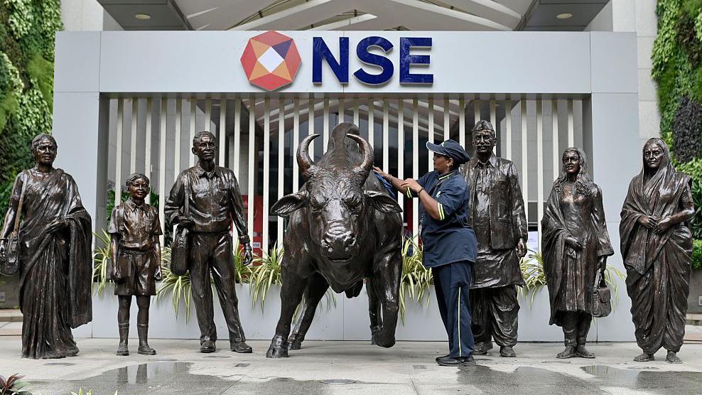 An employee cleans the metallic bull sculpture at the NSE headquarters. There are several other metallic sculptures of men and women around the bull. 