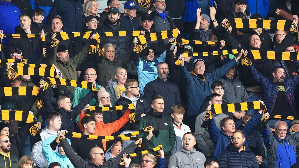 Sheffield Wednesday fans holding up black and gold scarves at a recent Hillsborough match
