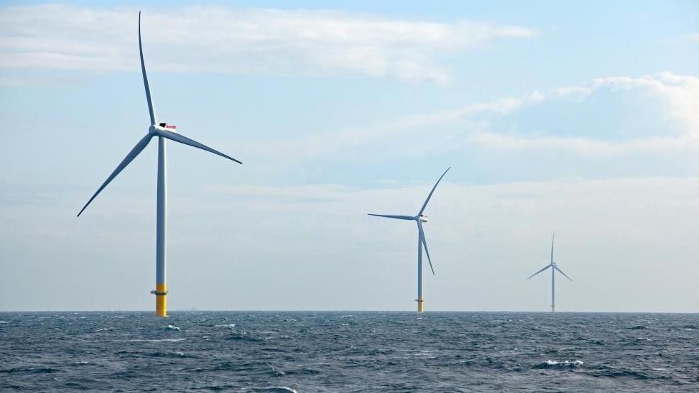 Three offshore wind turbines in the North Sea. Blue sky with clouds