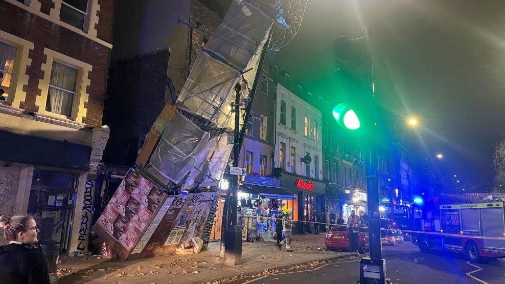 A tower of scaffolding partially collapsed onto Bethnal Green Road, with police and fire crews in attendance, 24 November