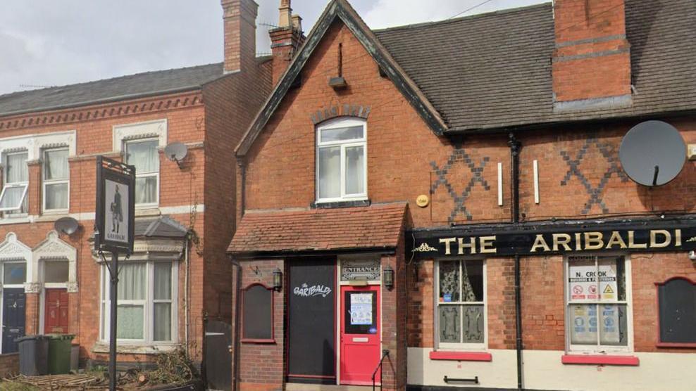 Red brick building with black tiles, black detailing on the walls and a red door