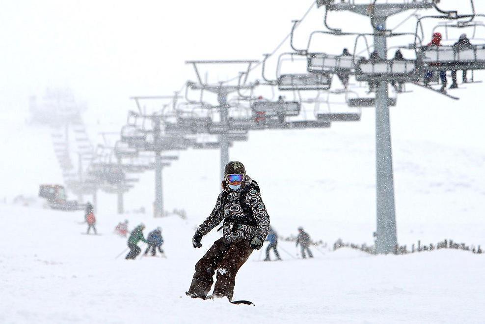 A snowboarder with a chairlift and skiers behind them.