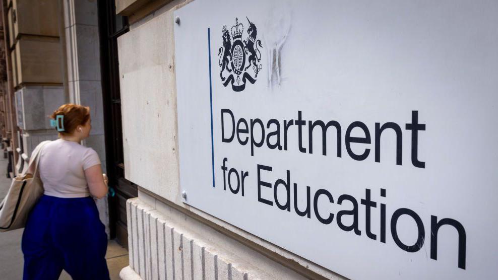 A woman on the left walking into a building, with a sign on the right reading "Department for Education".