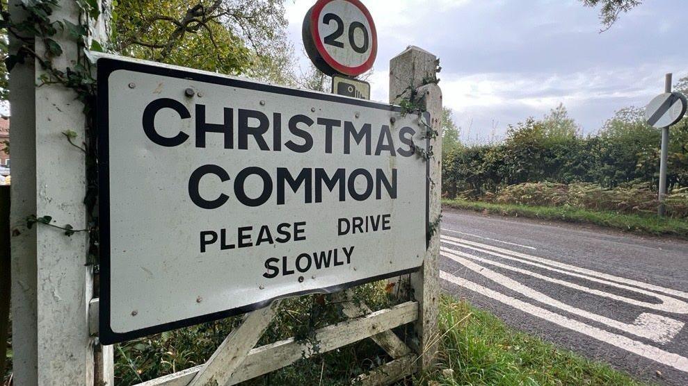 A roadsign alongside a road, saying "Christmas Common Please Drive Slowly"