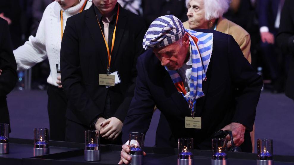 Auschwitz survivors light candles as they pay tribute to Holocaust victims at a ceremony commemorating the 80th anniversary of the death camp's liberation. In the picture, an elderly man wearing a blazer and striped hat and scarf - like the stripes worn by prisoners - is lighting a candle.