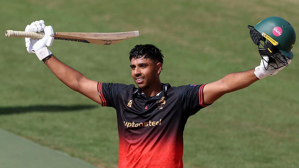 Rishi Patel beams with arms outstretched to celebrate his century