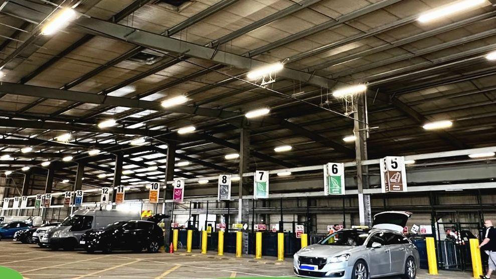 Cars are parked in a row at Fengate recycling centre. Their boots are open as people unload rubbish into areas, which have been labeled by what type of waste can be unloaded there.