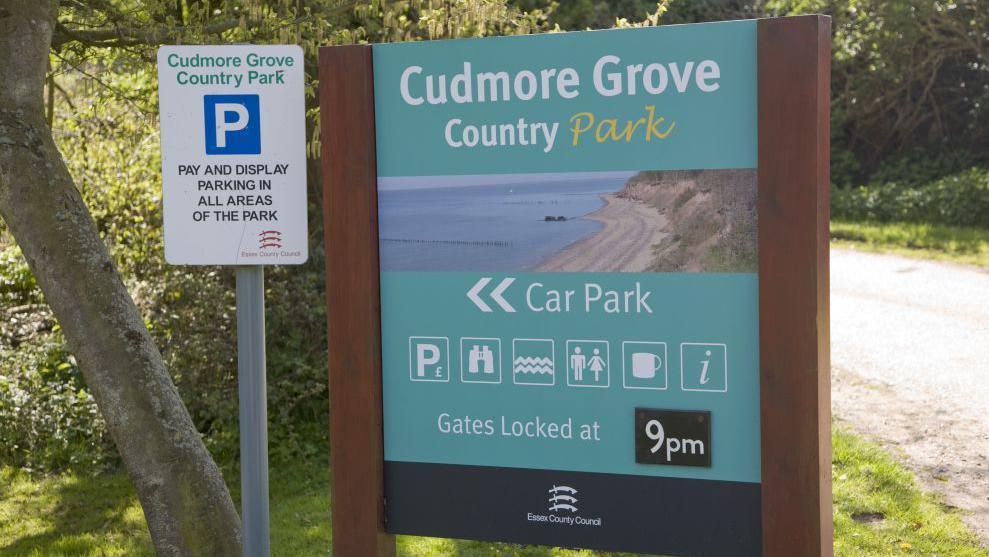 Entry sign for Cudmore Grove Country park. It advertises facilities such as parking, toilets and a cafe.