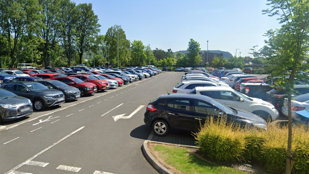 A car park on a sunny day, with dozens of cars parked there