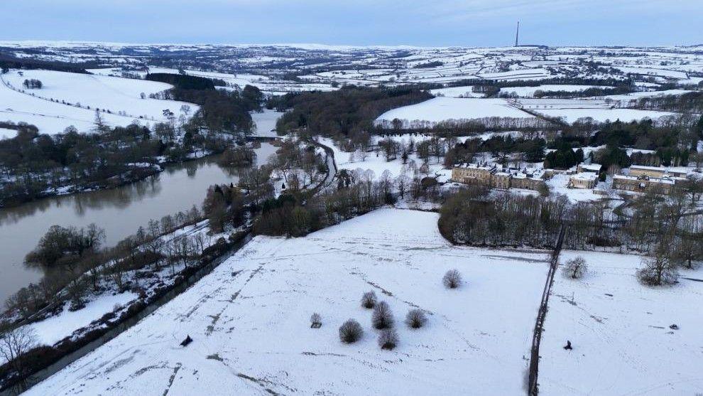 An aerial shot of snow-covered fields and country lanes, with a wide river on the left-hand side.