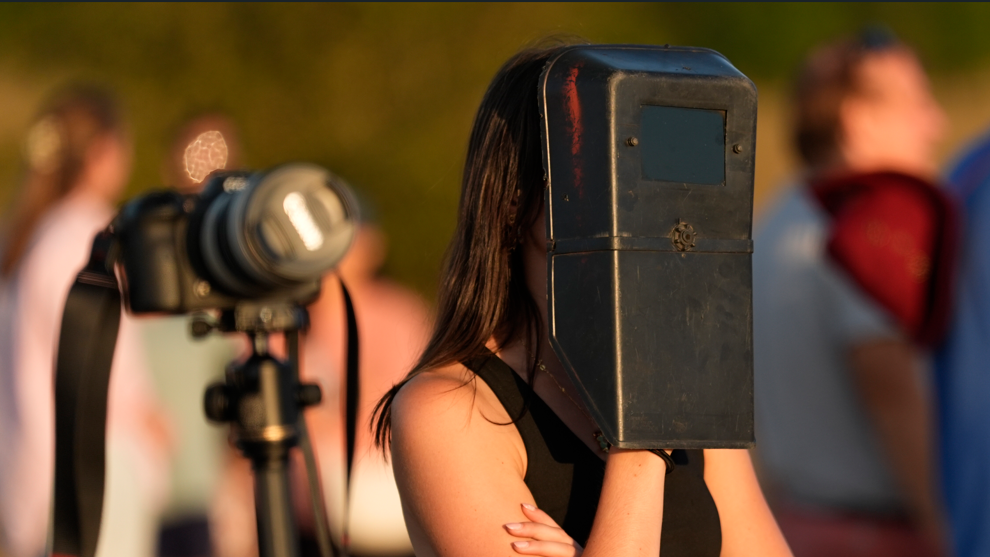 A woman is wearing a black welding mask looking at the sun