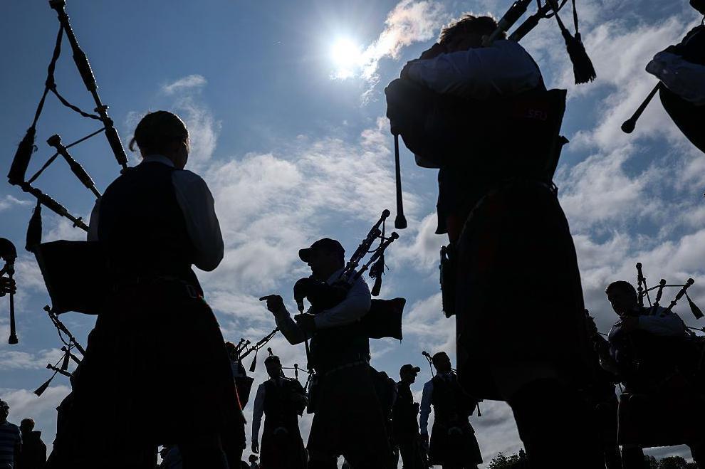 pipers in silhouettee against a blue sky. The sun is shining and there are white clouds in the sky