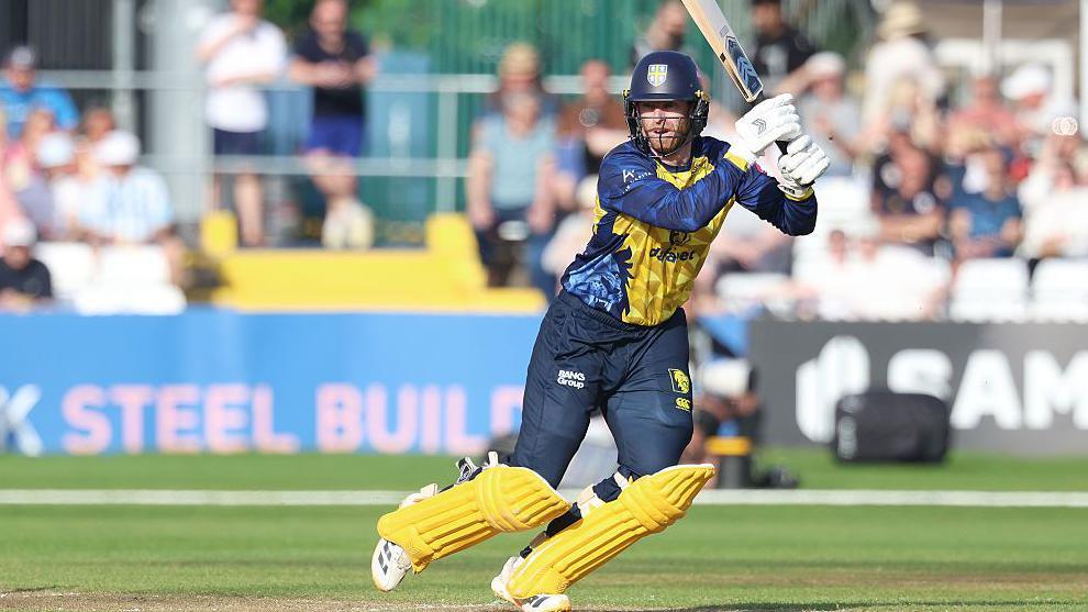 Graham Clark, in dark blue with yellow pads, setting off on a run after hitting the ball