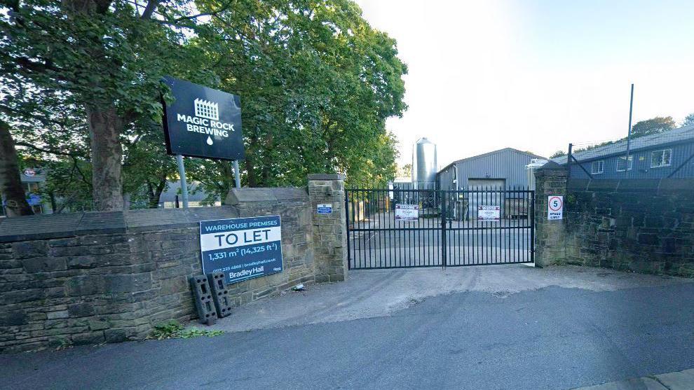 An entrance sign next to a wall and a gate which says Magic Rock Brewing.