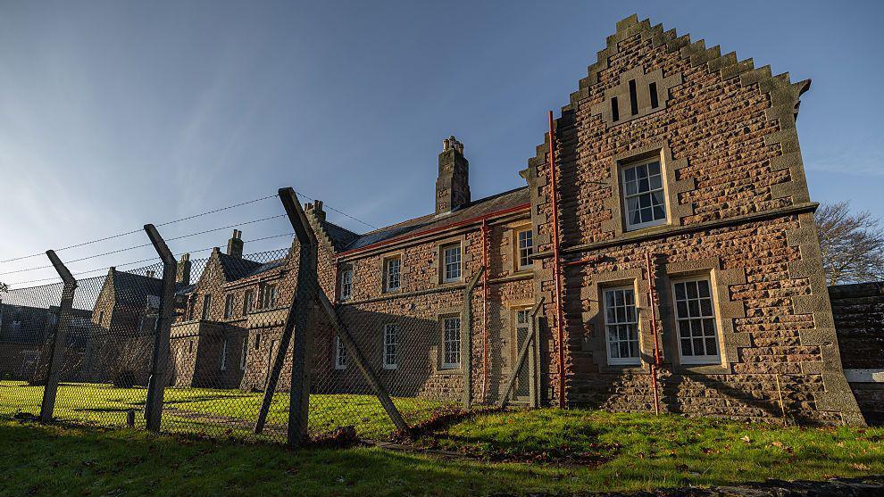 A red brick army barracks partly enclosed in a wire fence