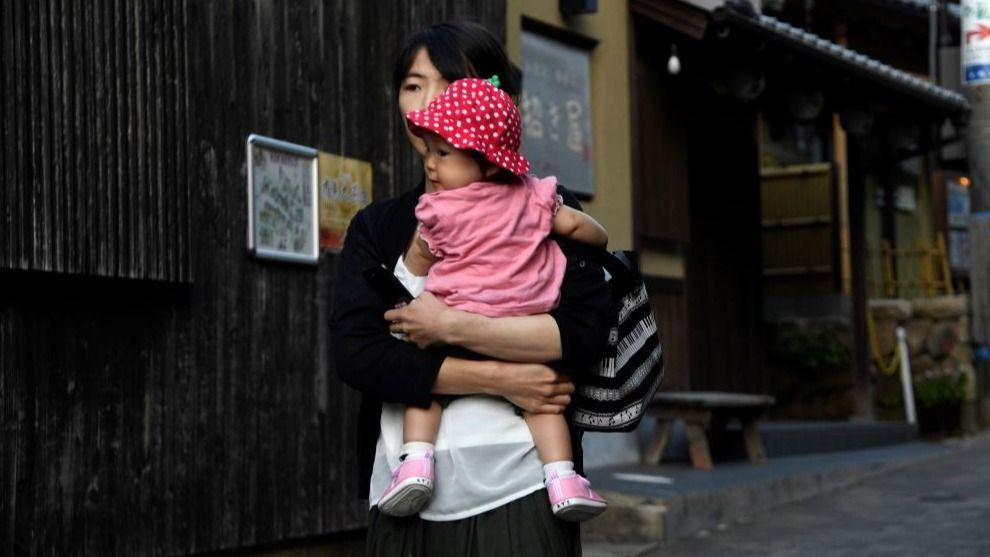 A woman in a black cardigan and white shirts holds a baby with a pink t-shirt and a strawberry hat on, in the hot spring town of Arima Onsen on the outskirts of Kobe 