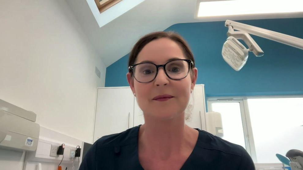 A woman who is wearing glasses and a navy top. She has brown hair.