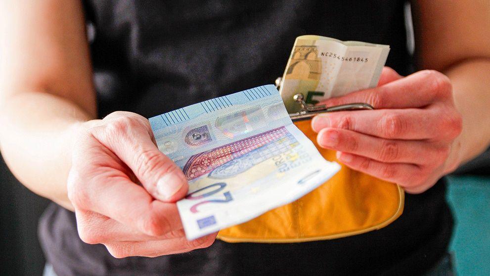 Woman's hands taking a 20 euro note and five euro note out of a purse