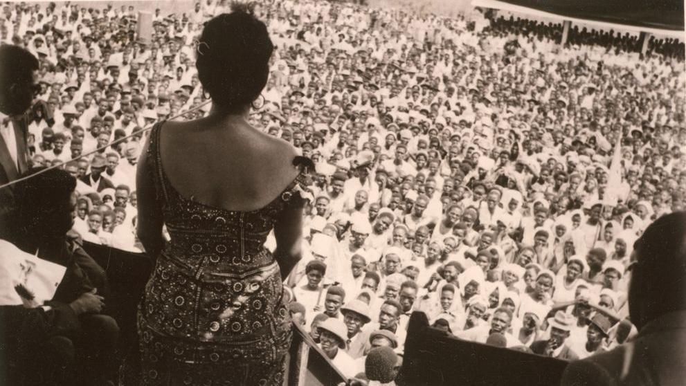 Wearing a patterened dress, Andrée gives a speech to a large crowd of men and women at a rally in the Democratic Republic of Congo